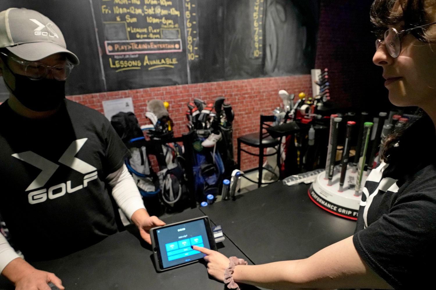 X-Golf manager J.W. Park, left, helps Ashley Moreno to check out at X-Golf indoor golf in Glenview, Ill., Friday, Jan. 20, 2023. Tipping fatigue, it seems, is swarming America as more businesses adopt digital payment methods that automatically prompts customers to leave a gratuity.