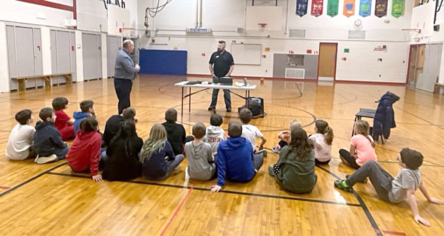 EOS/ESD Association, Inc.’s Business Development Manager Brennan Pimpinella, standing right, speaks recently to J.D. George Elementary School Principal Gary Bissaillon, standing left, and Science Club students at the Verona school about electrostatic discharge.
