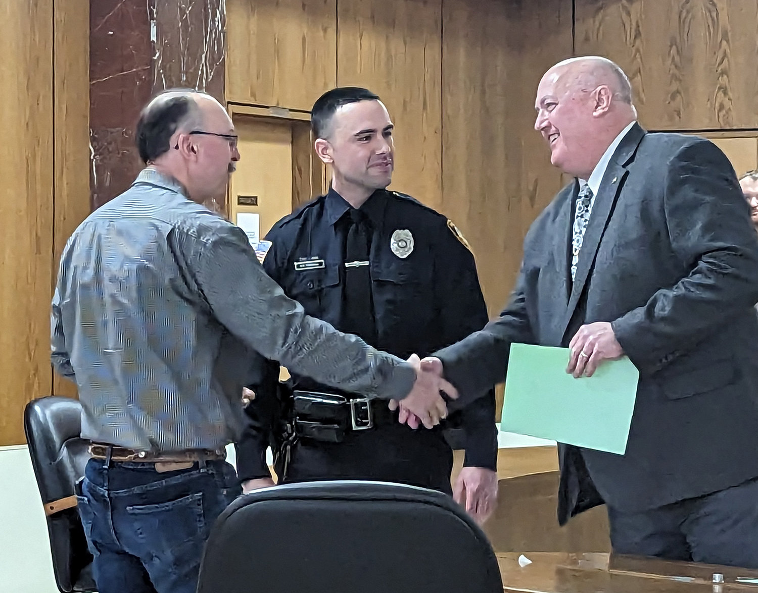 Utica Police Chief Mark Williams, right, shakes hands with the father of newly promoted sergeant Kyle Piersall, center, in Utica on Friday.