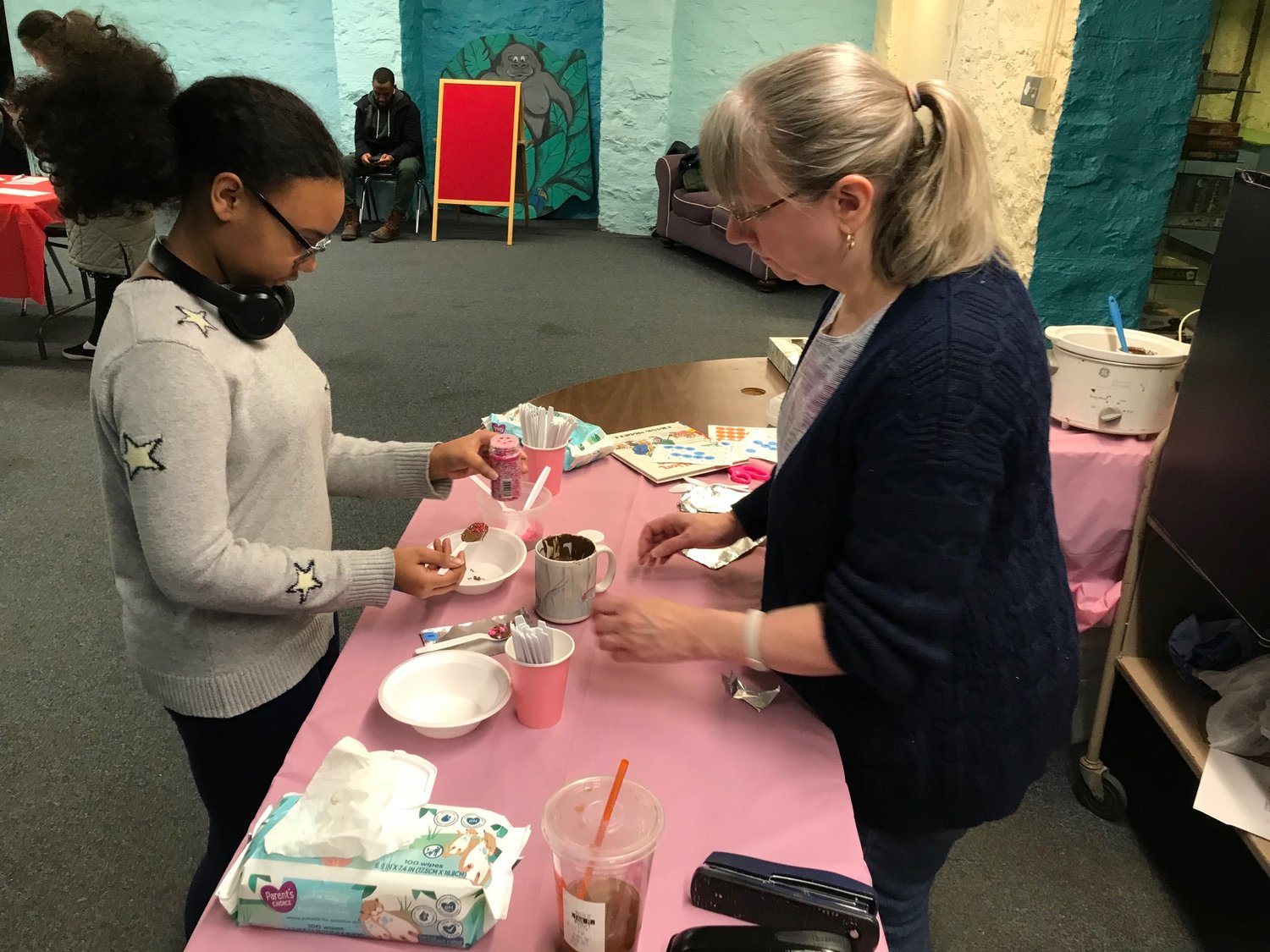 Jayla Wiggins, left, coats a plastic spoon with chocolate and sprinkles while Lisa Renz supervises Saturday, Feb. 11 during a special Valentine's Day children's program at the Utica Public Library.