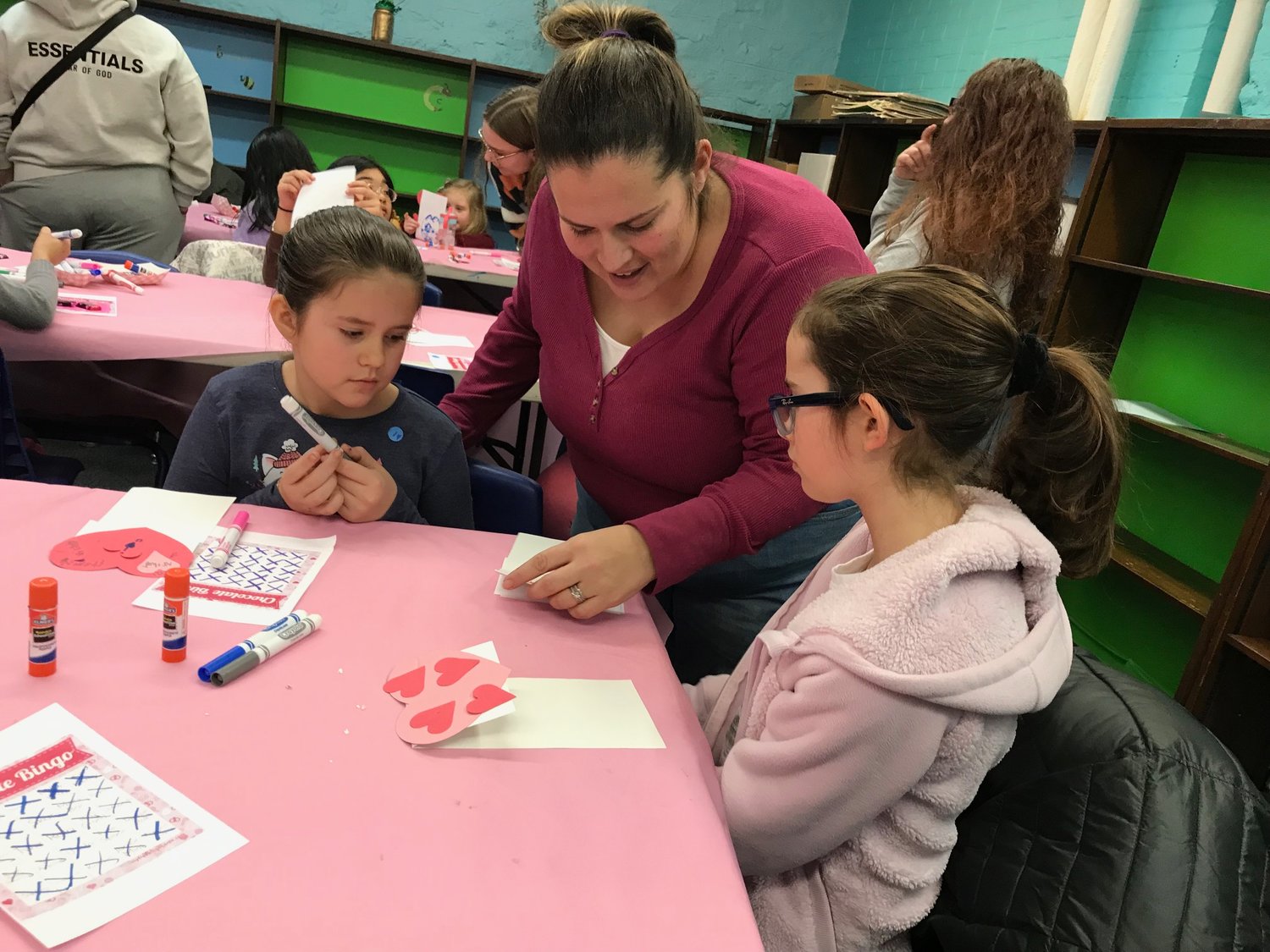 Becca Swalgin, center, takes a peak at the Valentine's Day crafts made by daughters Victoria, left, and Gabby Saturday, Feb. 11 during a special children's program at the Utica Public Library.