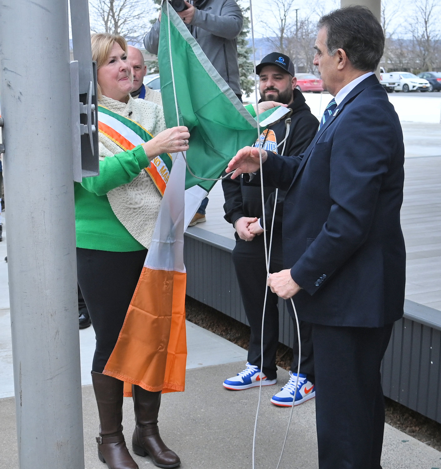 READY TO RISE — Colleen Kain Martin, left, gets some assistance from Mayor Robert Palmieri, as she gets ready to raise the Irish flag on Wednesday outside of Utica City Hall.  Martin’s ceremonial duties are just beginning as she will also serve as the grand marshal of the city’s upcoming St. Patrick’s Day Parade.