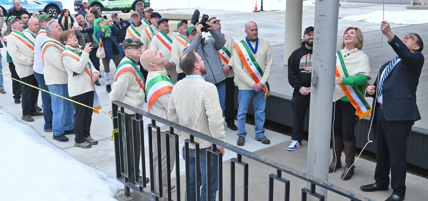 GOING UP — Spectators watch and take pictures and videos on their phones as the Irish flag is raised during a ceremony at Utica City Hall on Wednesday.