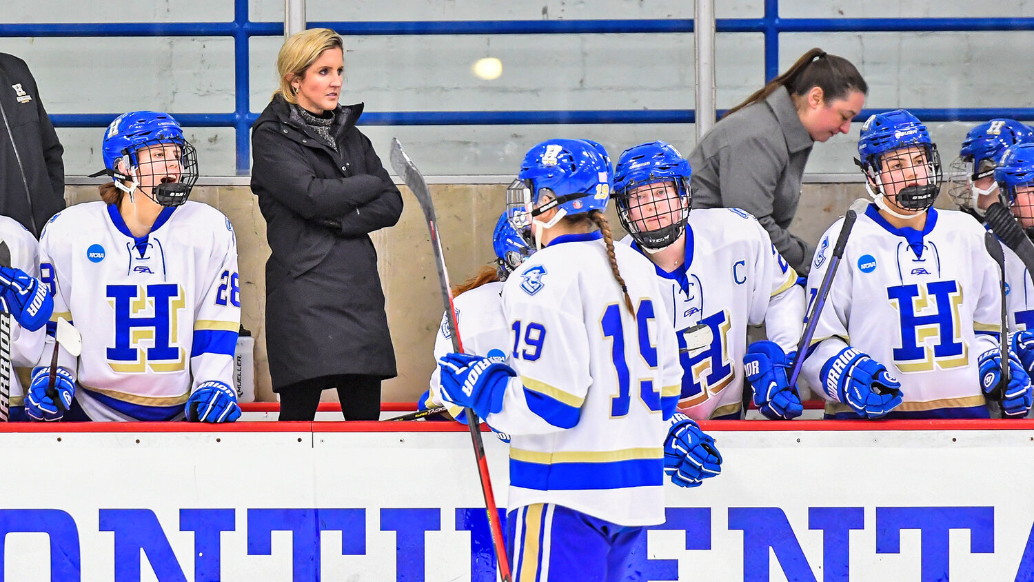 Hamilton College head women’s hockey coach Emily McNamara stands on the bench between players during the team’s NCAA Division III first round game at home against Nazareth College. McNamara has been chosen as the 2023 American Hockey Coaches Association Women’s Division III Coach of the Year.