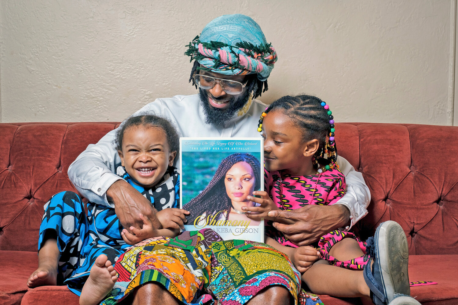 In this photo provided by Henry Danner, Omari Maynard sits with his children, Khari, left, and, Anari, holding a photo of their late mother, Shamony Gibson, at home in the Brooklyn borough of New York on April 9, 2022.