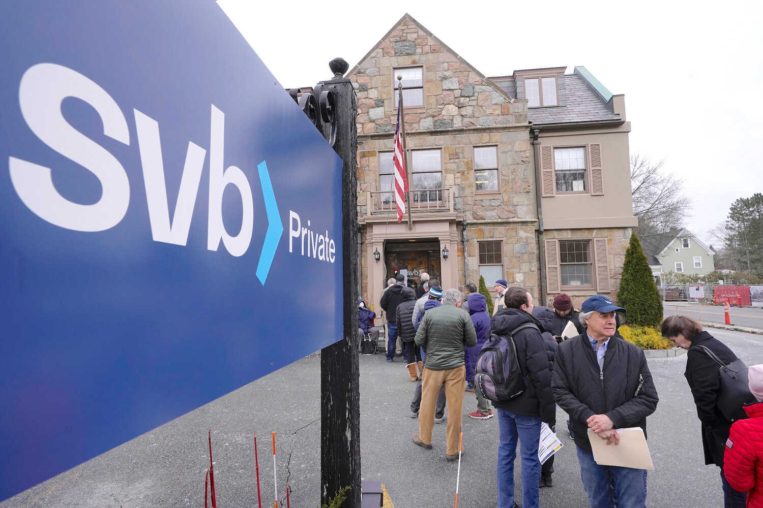 Customers and bystanders form a line outside a Silicon Valley Bank branch location, Monday, March 13, in Wellesley, Mass.