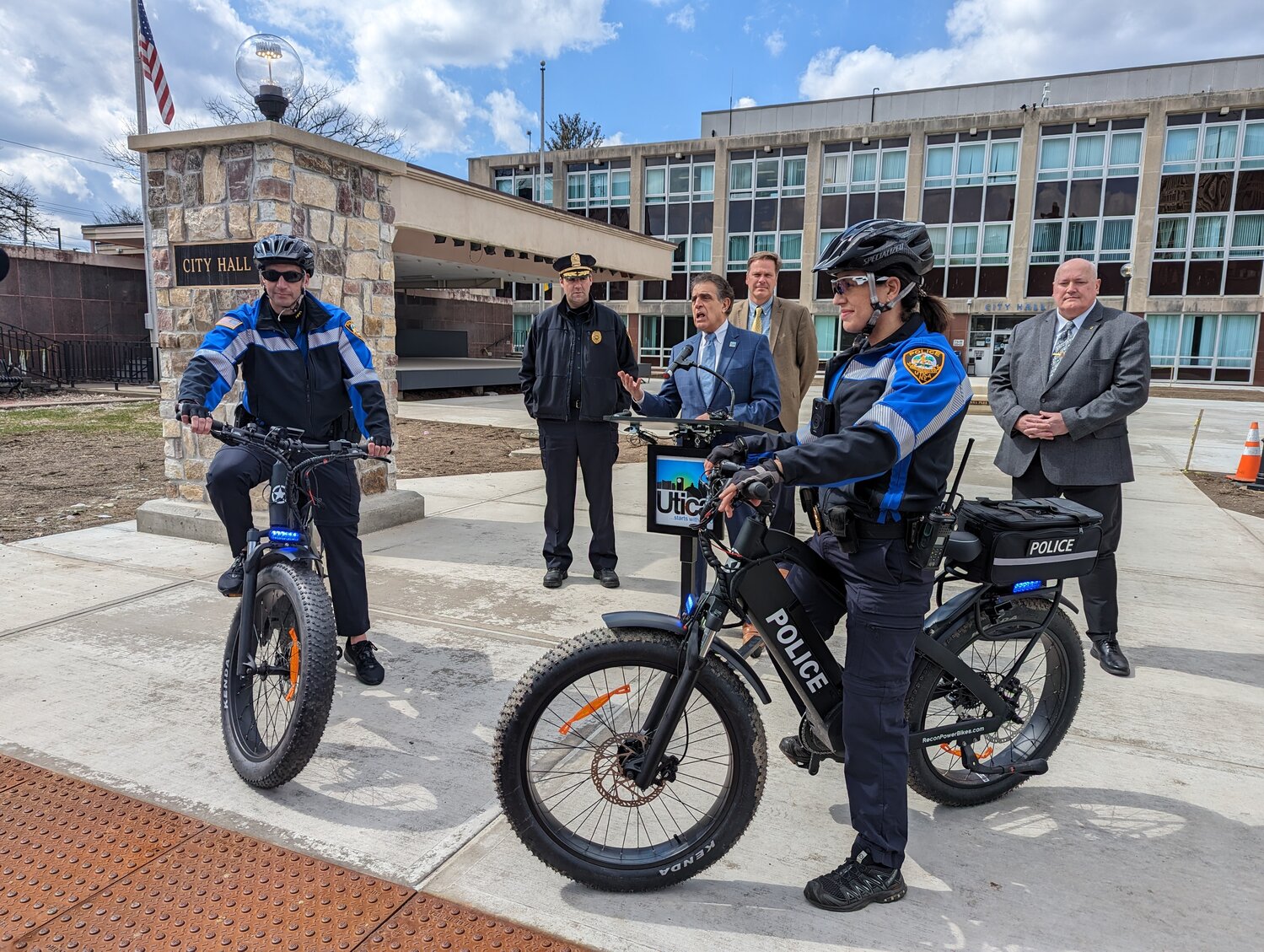Two Utica police officers show off the new, heavy duty electronic bicycles that will be going on patrol in Utica parks. From left: Sgt. James Laurey, Capt. Brian Bansner, Mayor Robert Palmieri, Deputy Chief Ed Noonan, Inv. Shannon Acquaviva, and Utica Police Chief Mark Williams.