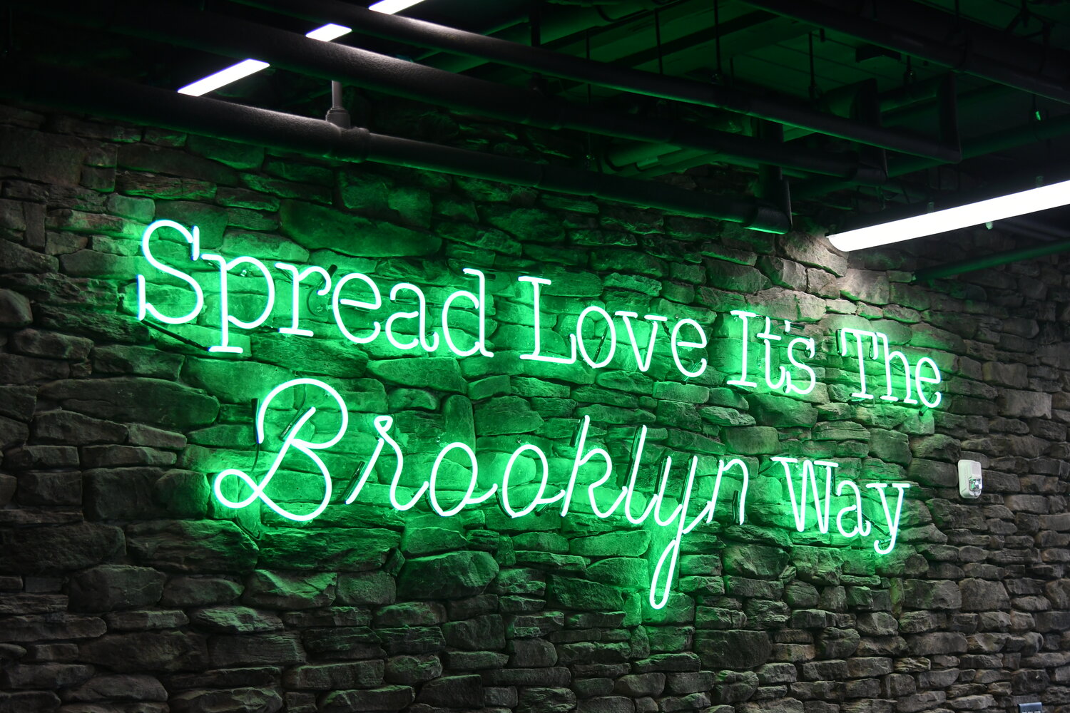 A neon sign greets people in line as they wait to place their order. The sign reads "Spread Love It's The Brooklyn Way."