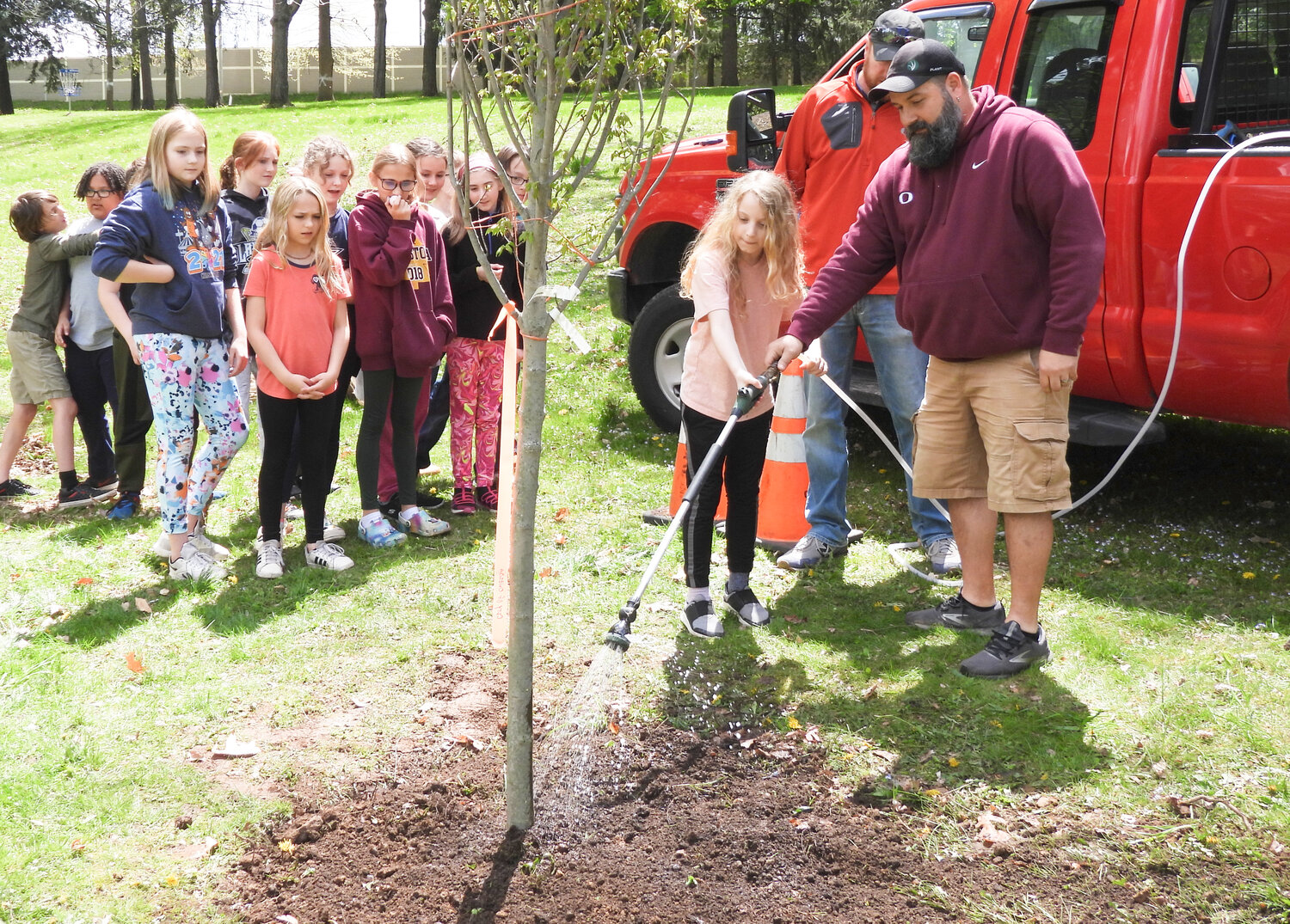 Maintenance Head Steven Crawford instructs Senac Street Elementary students on how to water the newly planted tree in Allen Park on Friday, May 5