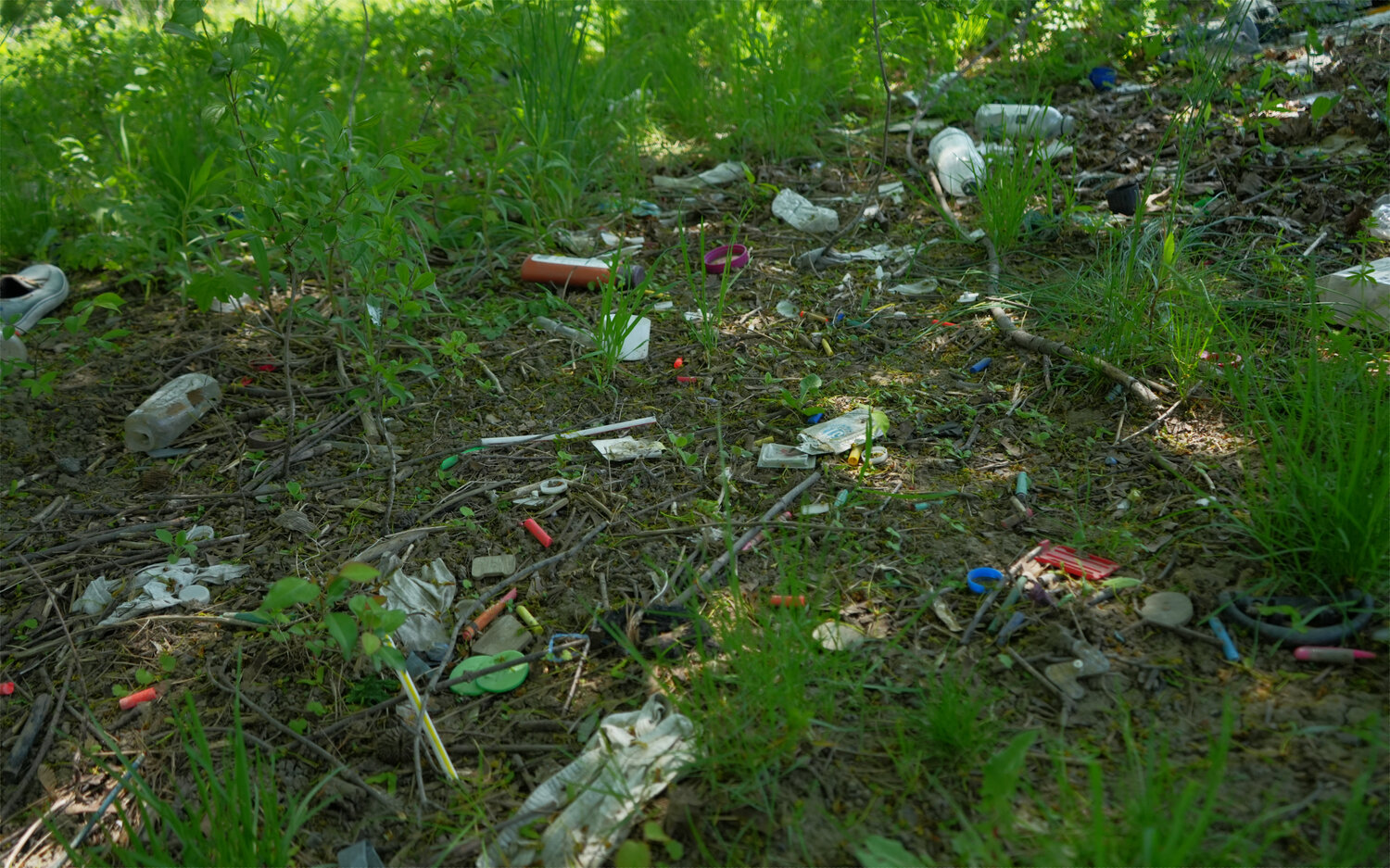 A couple hundred yards from a homeless encampment, personal items are found scattered around a tree, such as: crayons, water bottles, shows, body wash and cigarettes.