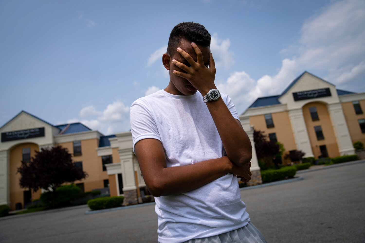 Mohamed, a 19-year-old fleeing political persecution in the northwest African country of Mauritania, poses for a photo that obscures his face to protect his identity, outside the Crossroads Hotel, before heading into town for a work opportunity, Monday, May 22, 2023, in Newburgh, N.Y.  Mohamed is one of about 400 international migrants the city has been putting up in a small number of hotels in other parts of the state this month to relieve pressure on its overtaxed homeless shelter system.