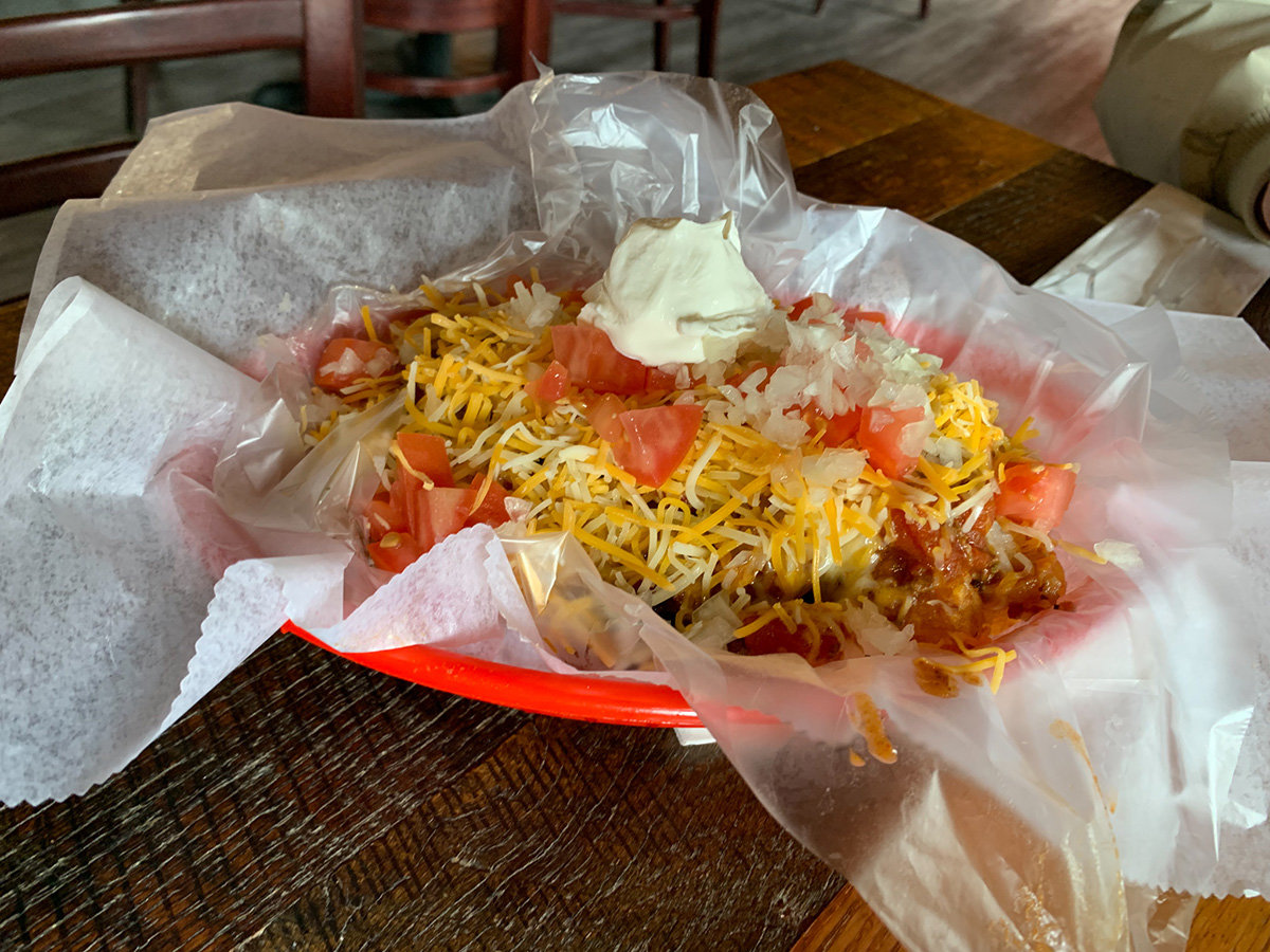 The baked tots are smothered in homemade chili, cheddar cheese, chopped onions and crispy bacon, all topped with diced tomatoes and a dollop of sour cream.