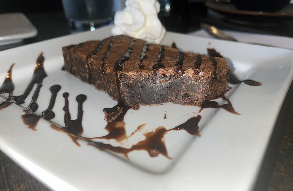The brownie was served cold and drizzled with chocolate syrup and a side of whipped cream.