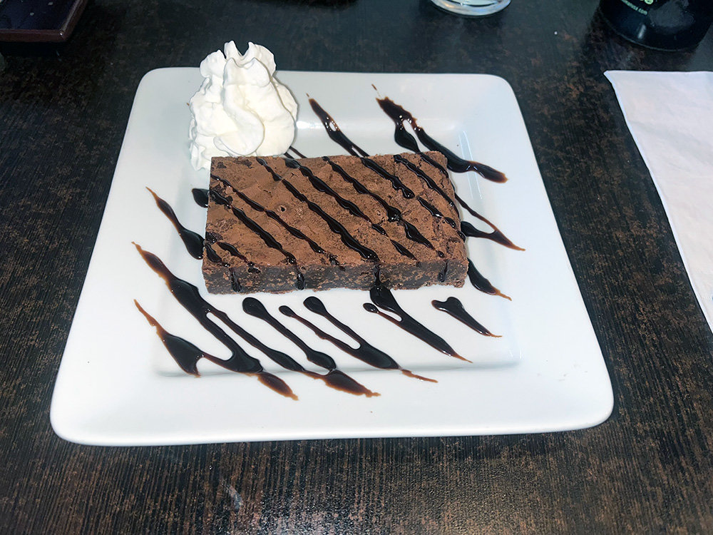 The brownie was served cold and drizzled with chocolate syrup and a side of whipped cream.