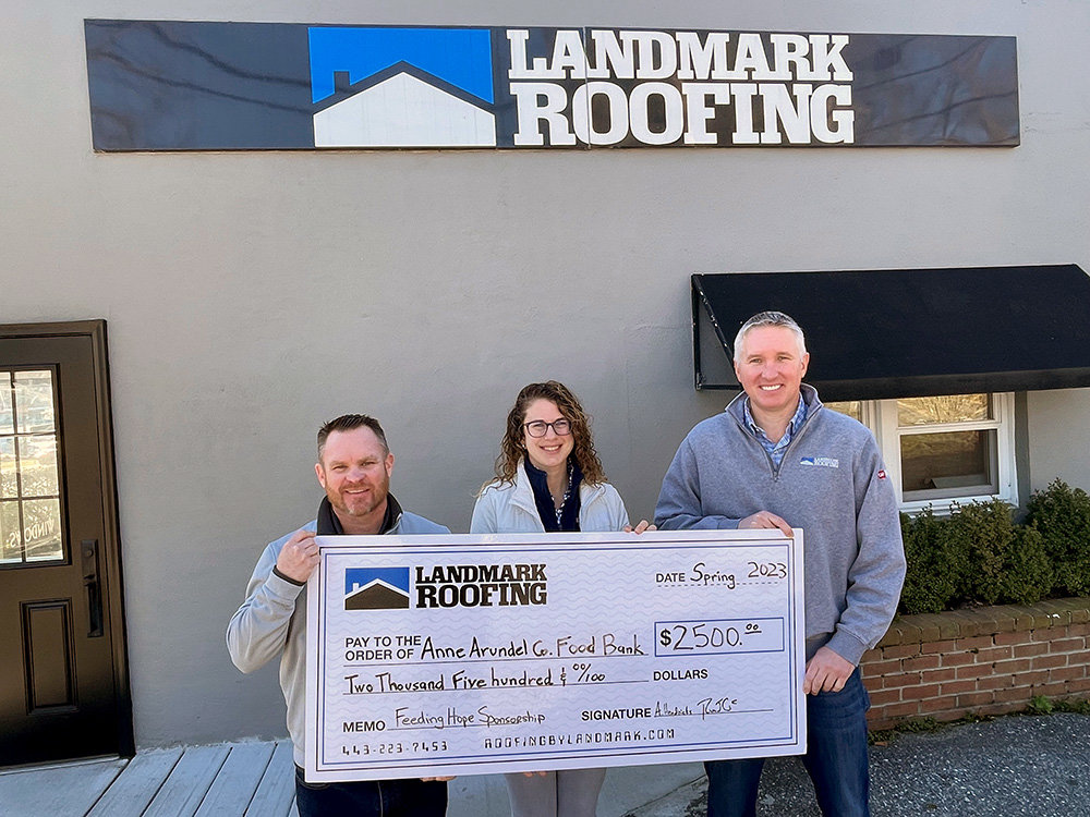 Landmark Roofing owners Rob Calhan (left) and Artie Hendricks (right) presented a $2,500 check to Leah Paley, CEO of the Anne Arundel County Food Bank.