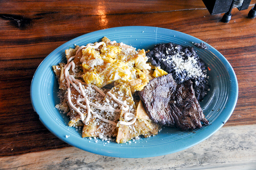 Chilaquiles are fried corn tortillas sauteed with grilled steak, onions, either salsa verde or salsa roja, and topped with queso fresco. They are served with two eggs and a side of black beans.