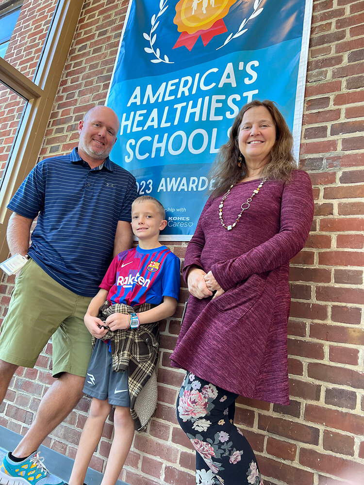 Rich Wiles, a physical education teacher at Severna Park Elementary School, posed in front of an America’s Healthiest Schools banner at the school’s entrance with third-grade student Bode Wiles and school counselor Katie McCord.
