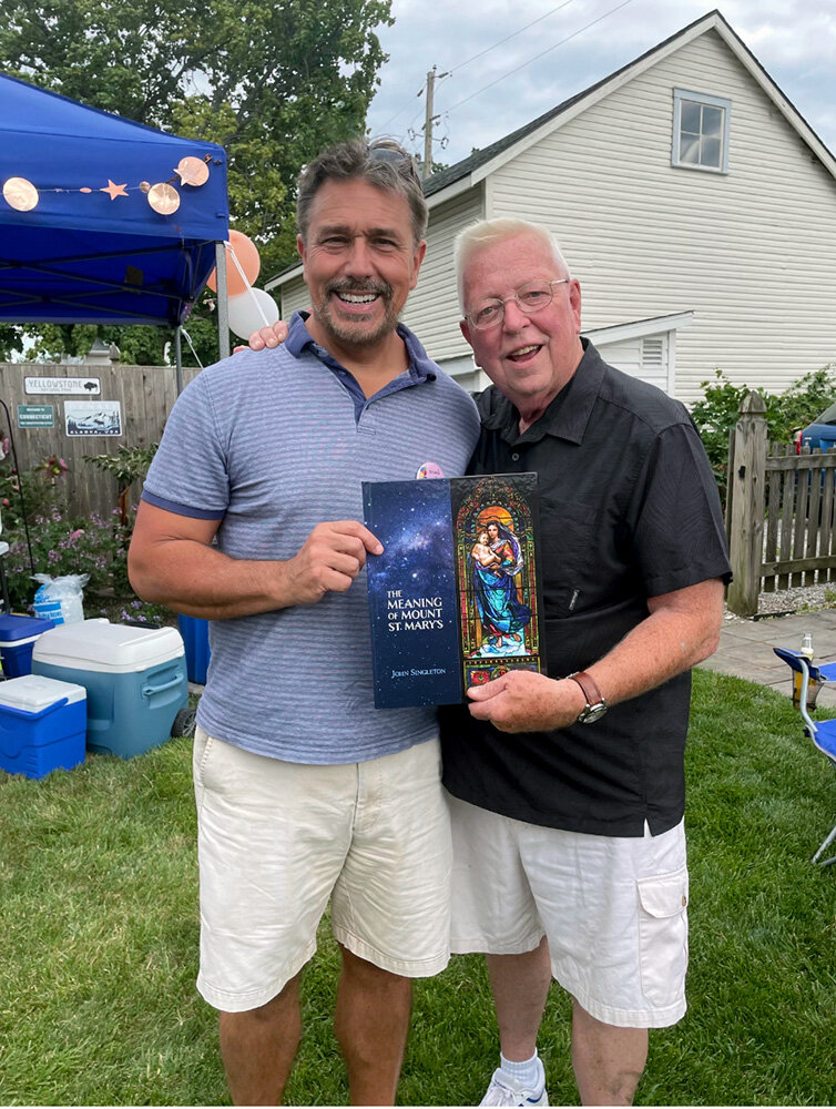John Singleton (left) and Mount St. Mary’s University President Emeritus Tom Powell posed with a copy of “The Meaning of Mount St. Mary’s.”
